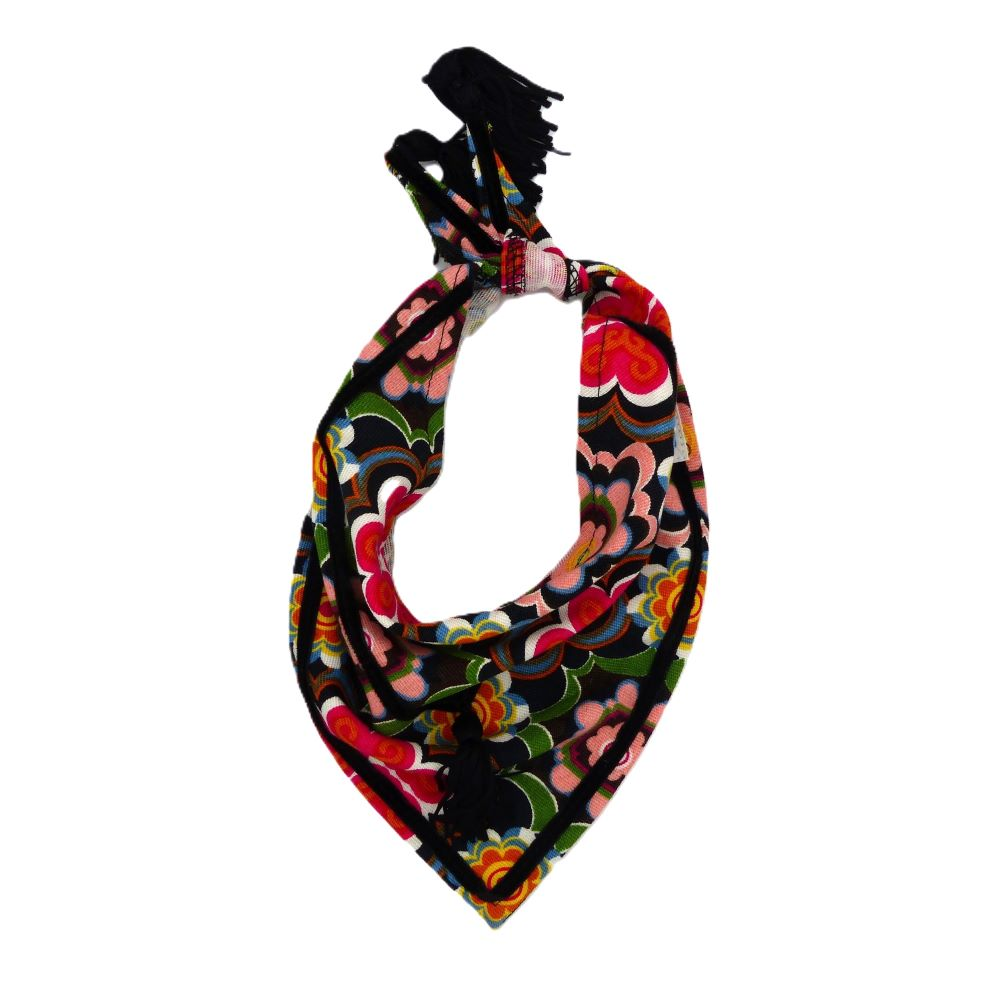 Bright floral print dog bandana with ribbon edging and tassels, displayed lying flat on a surface