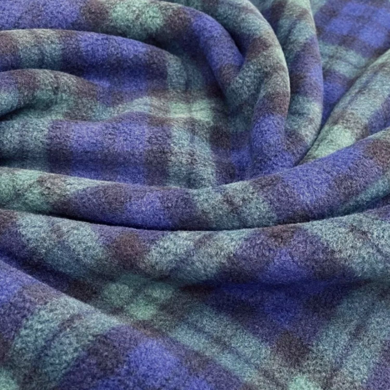 “Close‑up view of soft fleece fabric in a blue‑green tartan pattern, showing the fuzzy texture and intersecting plaid lines.”